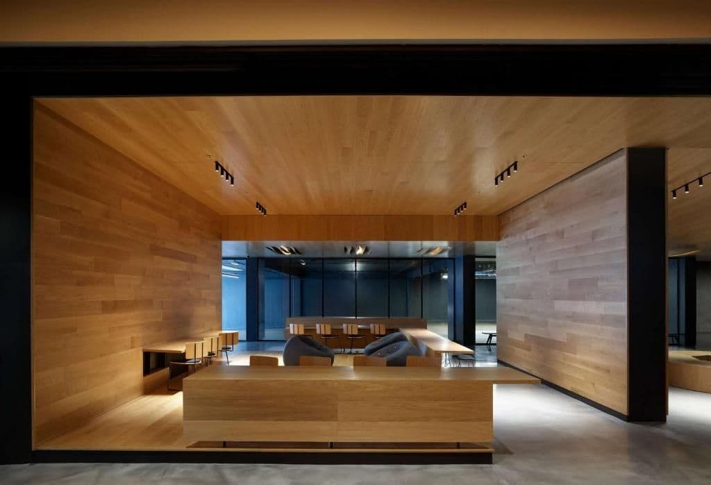 Modern corporate event venue with warm wooden walls, concrete floors, and diverse seating for collaboration.