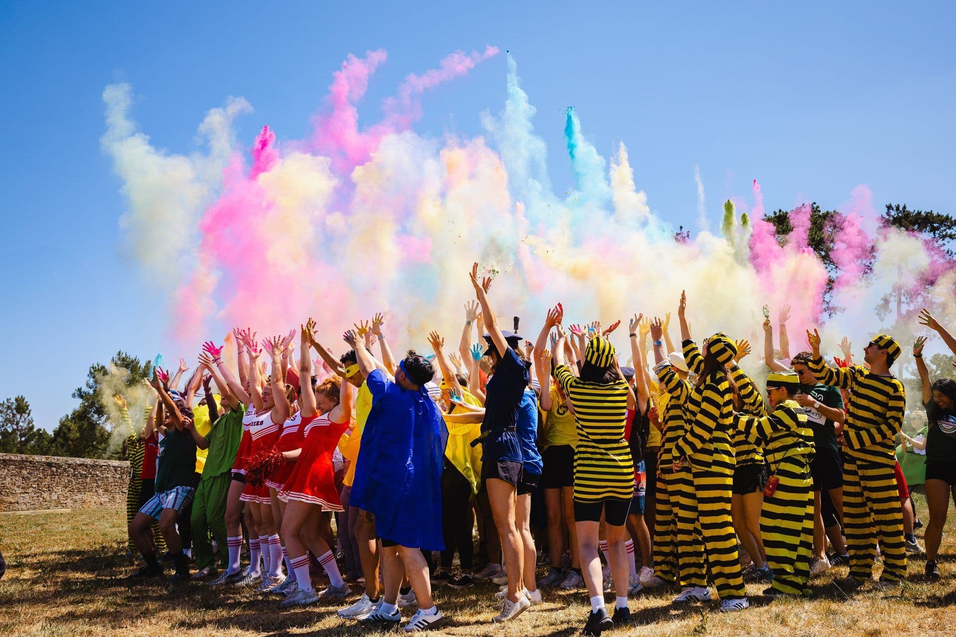 A large group of people in costumes celebrating with colorful smoke during an outdoor team building event.