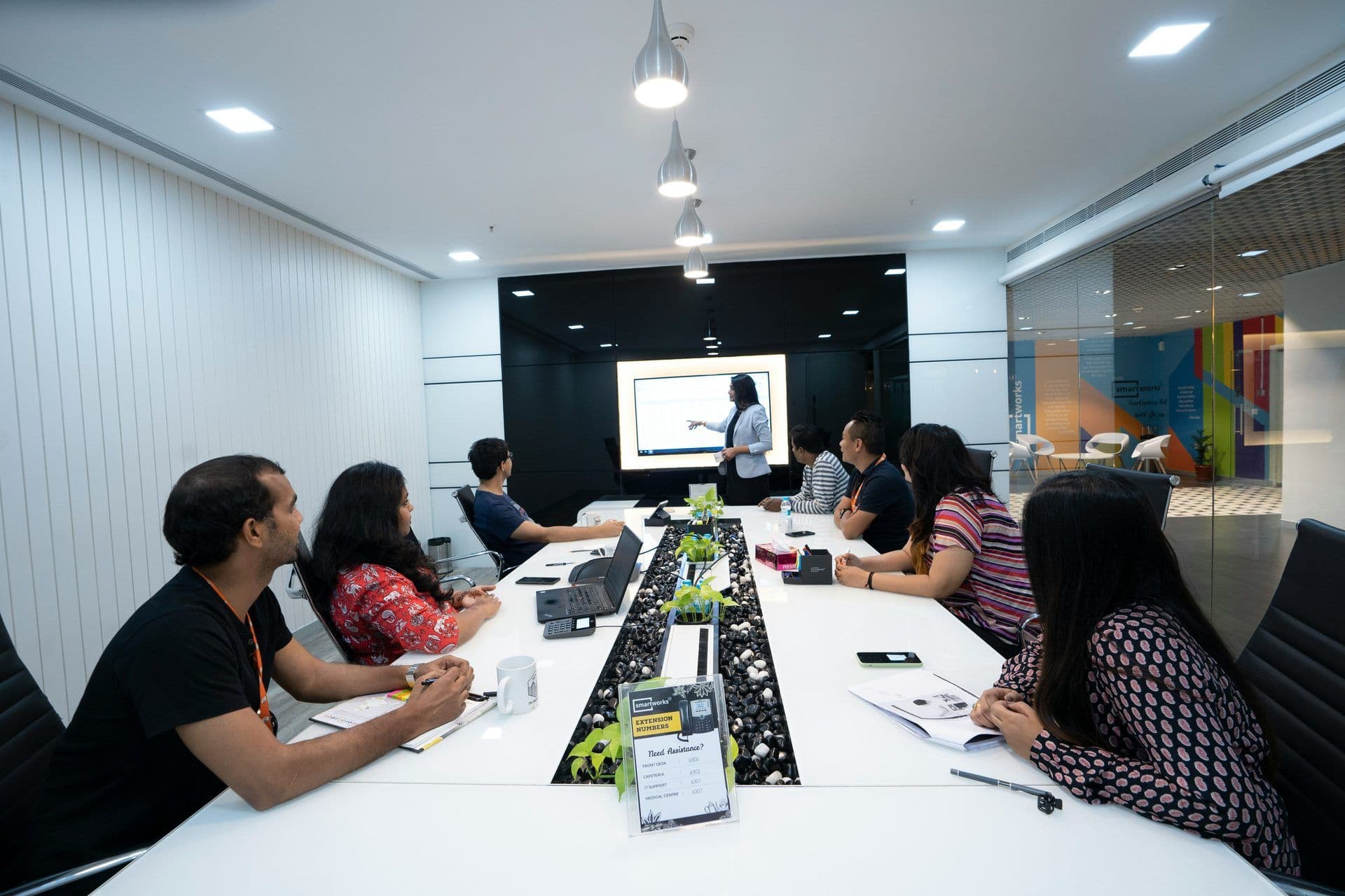 Professionals attend a corporate workshop in a modern boardroom with a presenter and large screen.