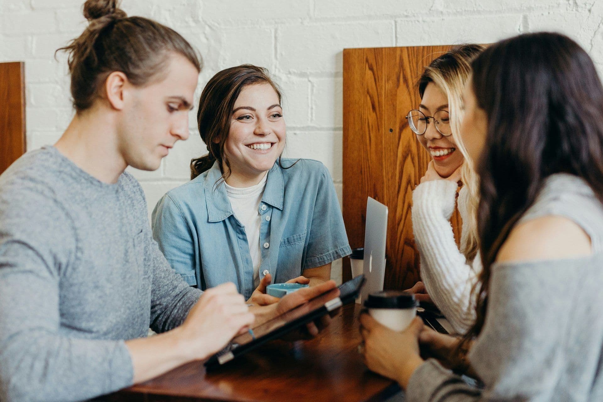 Four smiling colleagues discuss ideas around a table with coffee and technology during a corporate workshop.