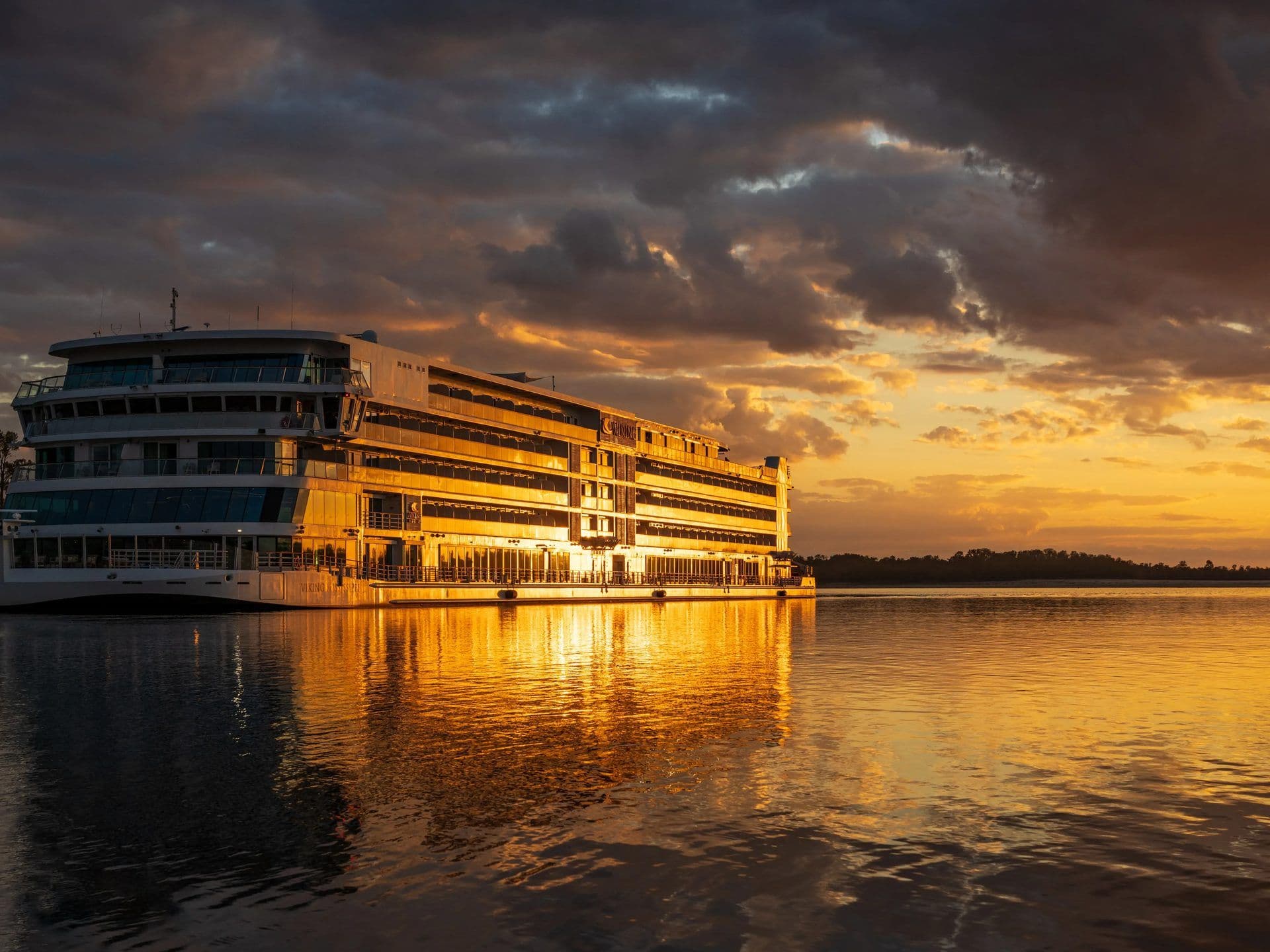 A large multi-deck Viking cruise ship glows golden on the Mississippi River at sunset