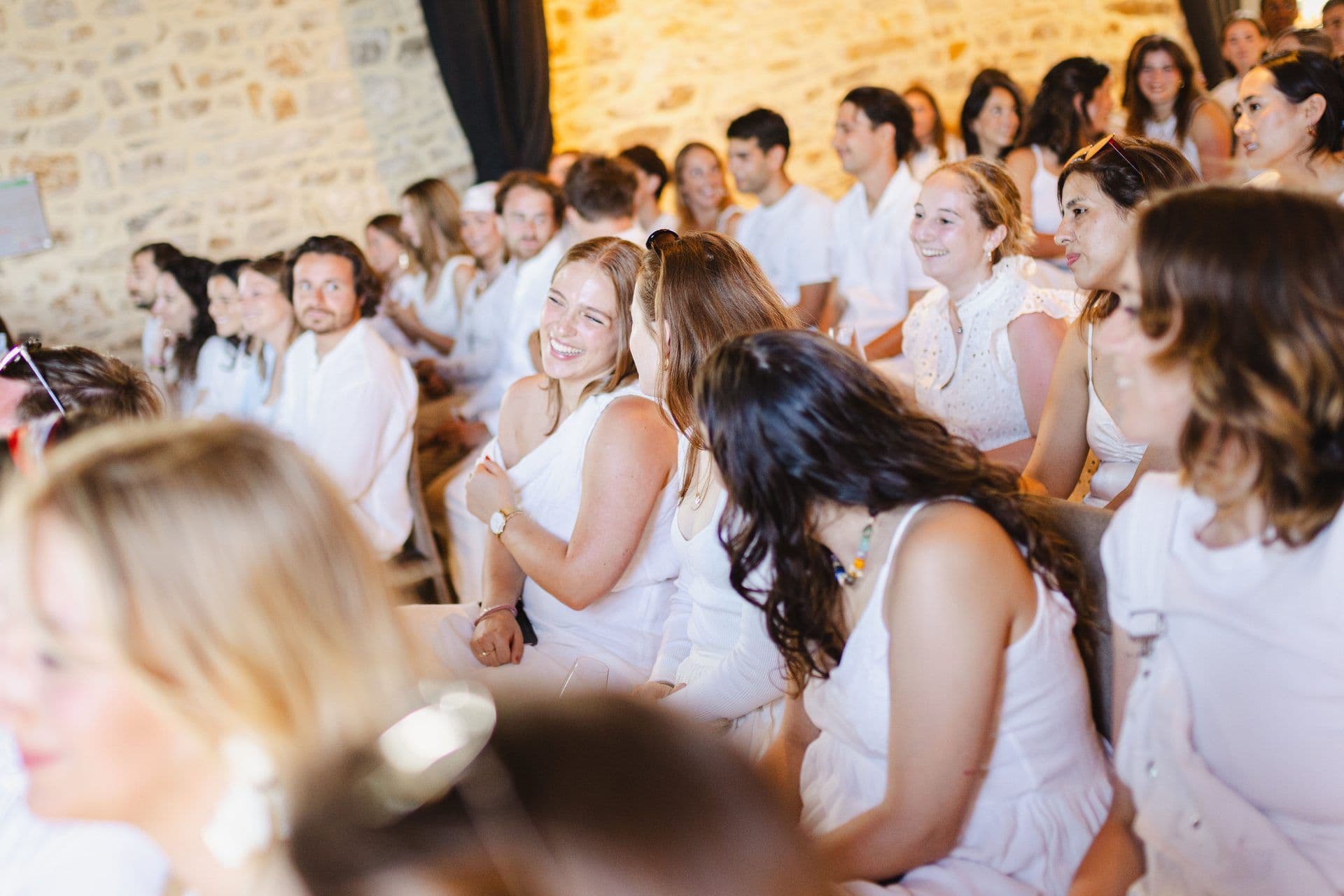 A large group of smiling colleagues in white attire attending a corporate seminar in a historic stone-walled