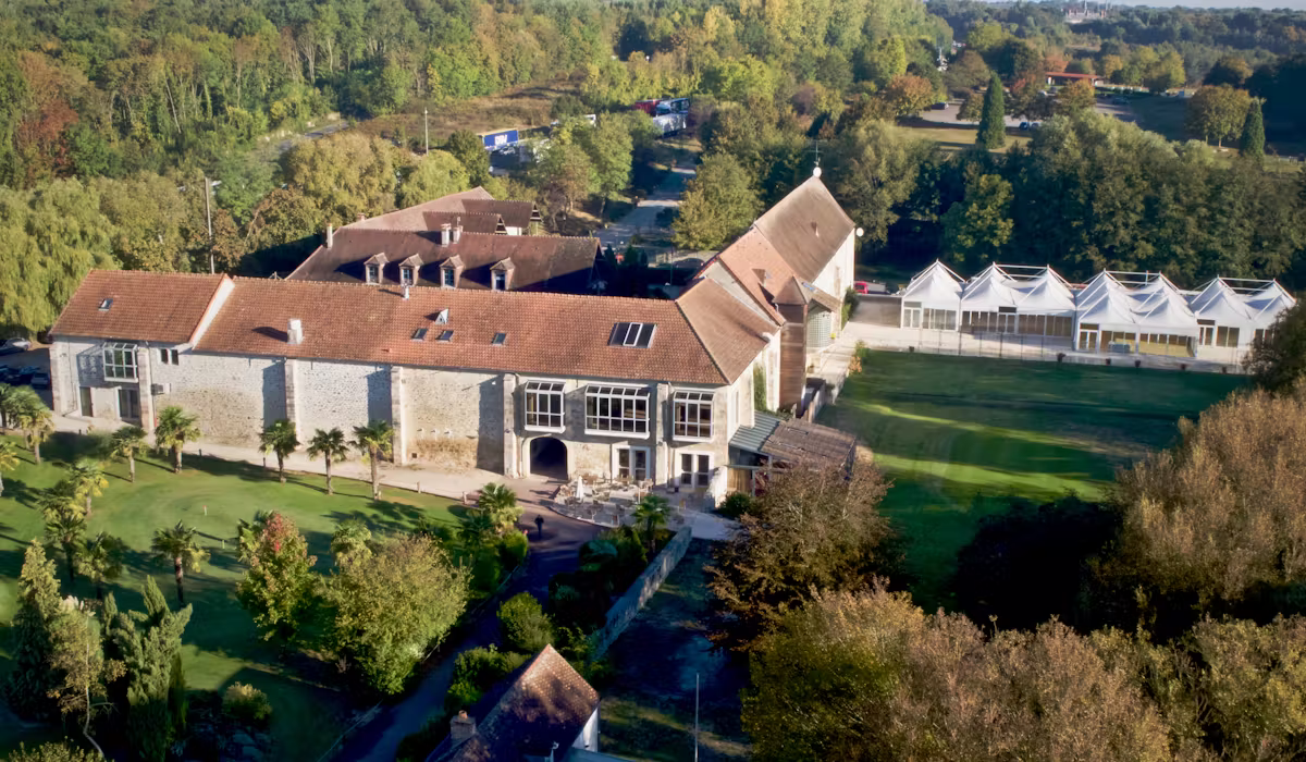 Aerial view of a historic corporate event venue with stone buildings, green lawns, and white tent spaces.