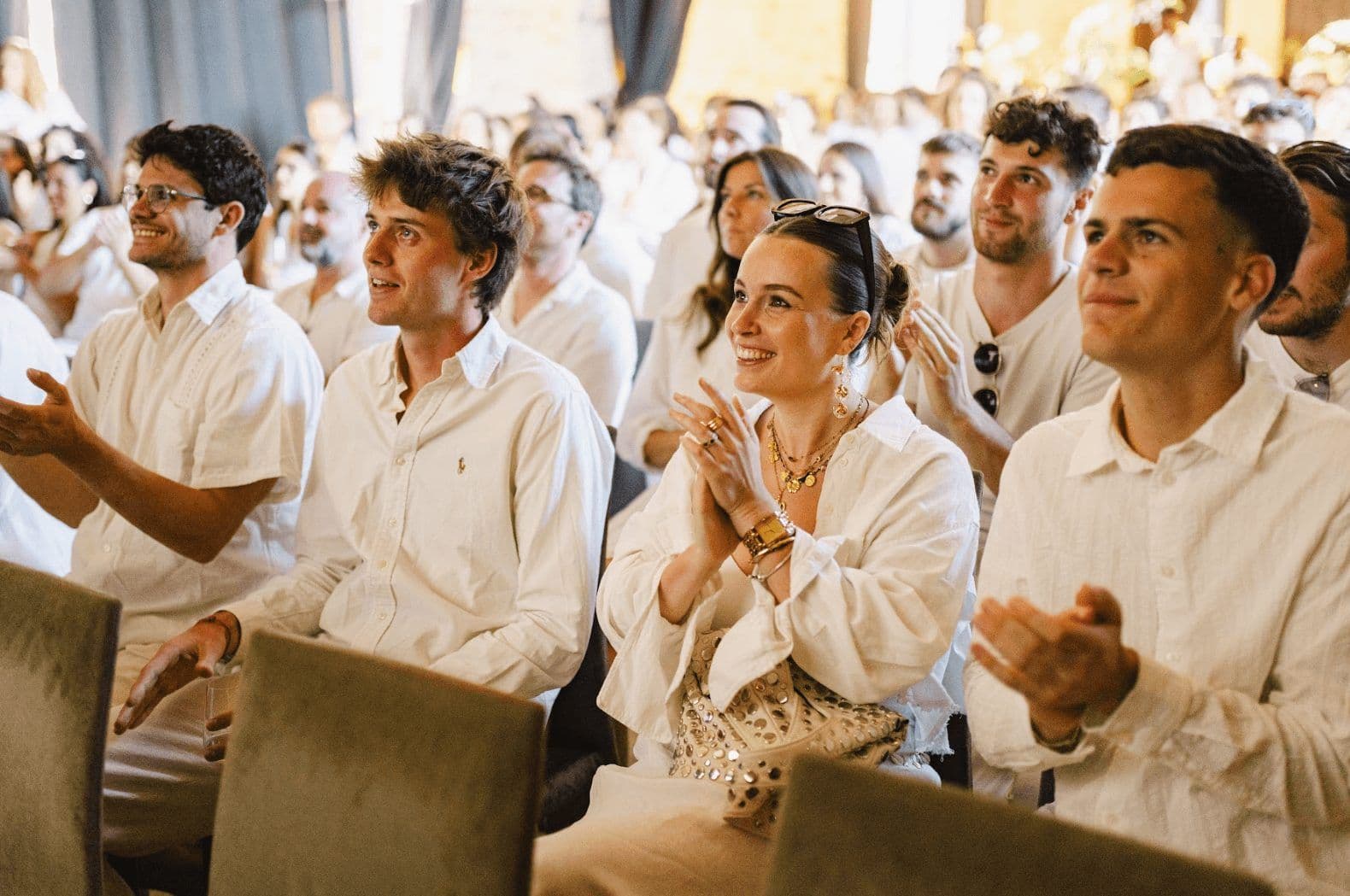 A group of smiling attendees in white shirts clapping at a corporate seminar or team building event.