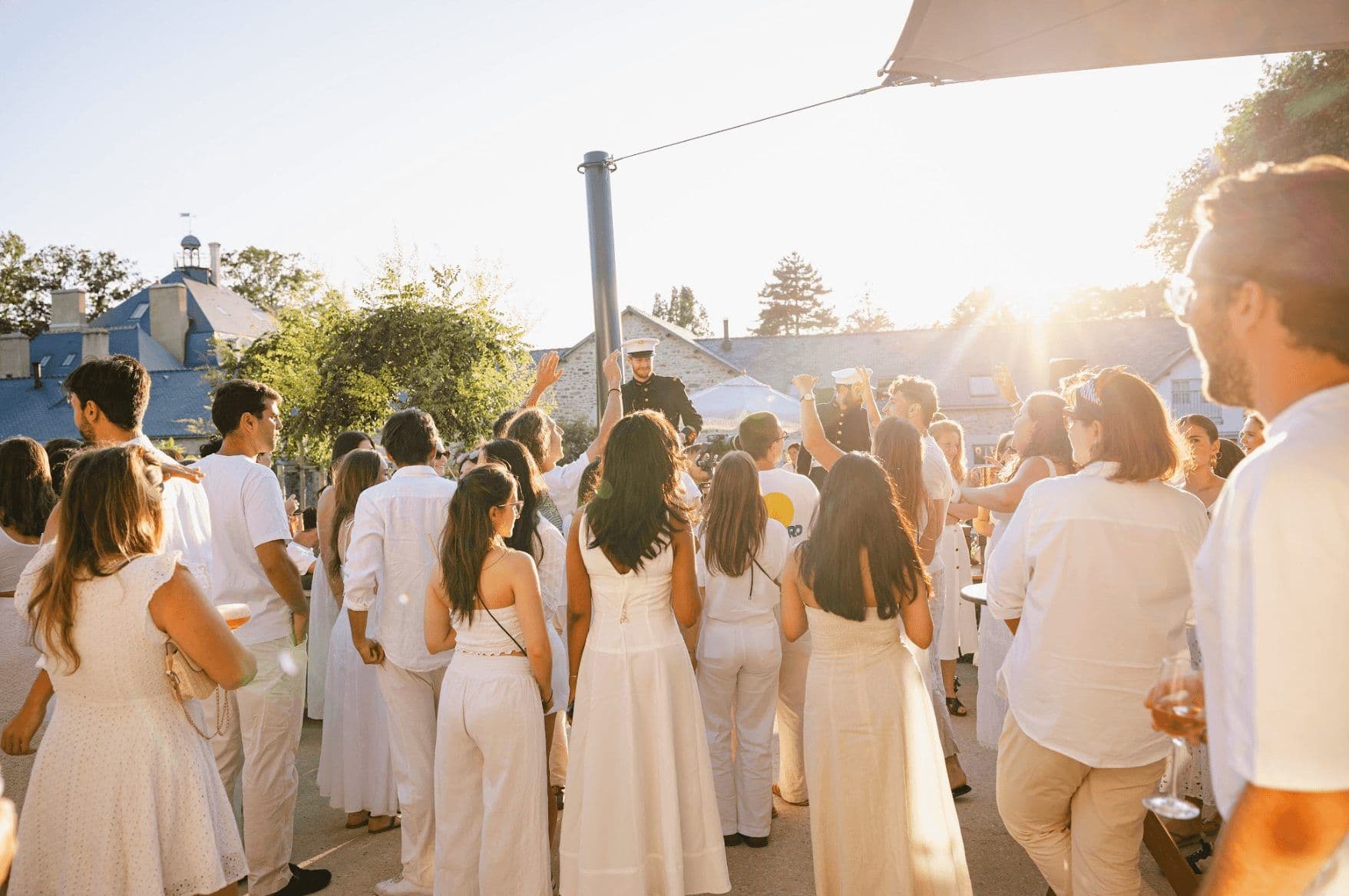 A large group enjoys an outdoor corporate cocktail reception at a historic venue during sunset.