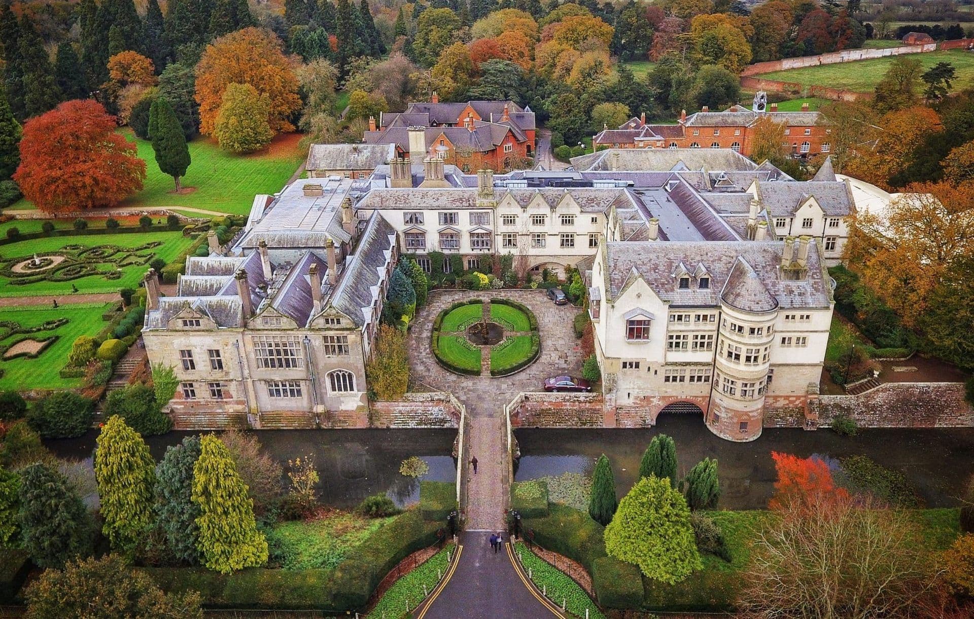Aerial view of Coombe Abbey, a historic corporate event venue with a moat and autumn gardens in the UK.