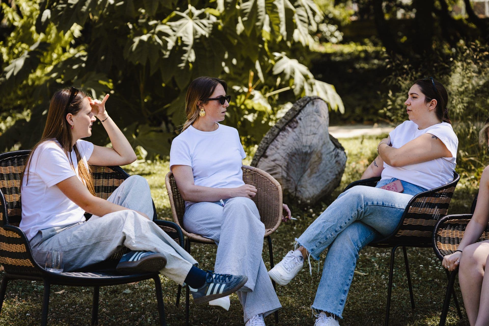 Three women in casual attire discuss outdoors in a lush garden, ideal for a team offsite or corporate retreat.