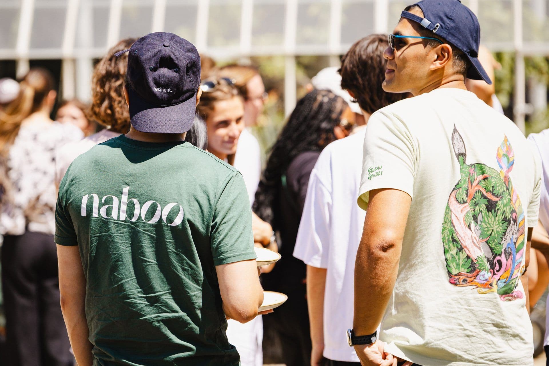 People networking outdoors at a corporate event, with one person wearing a Naboo t-shirt and holding plates.