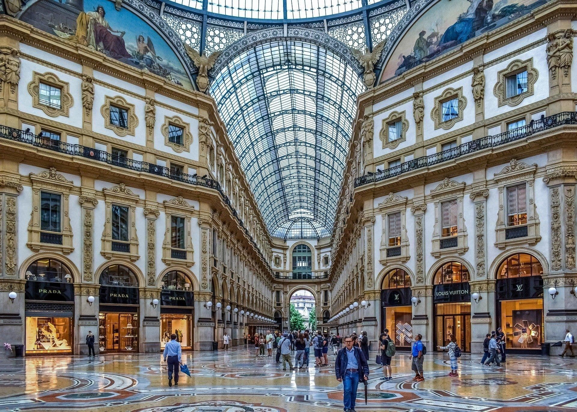 Ornate historic gallery in Milan featuring a vaulted glass ceiling and mosaic floor.