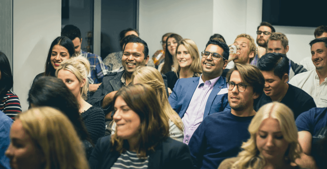 A diverse group of professionals smiling and engaged during a corporate seminar or workshop.