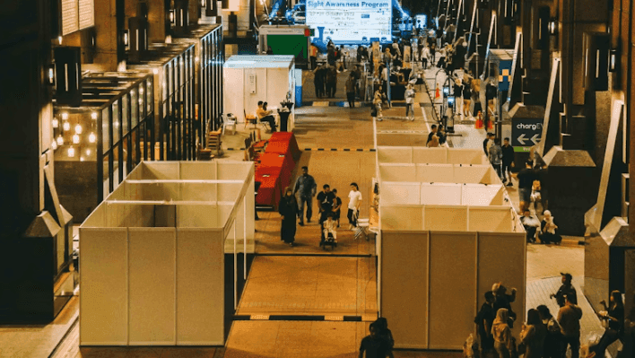 A bustling indoor event space with multiple exhibition booths and attendees at a 'Sight Awareness Program'.