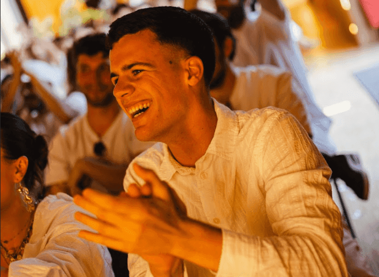 A smiling man in a light shirt claps enthusiastically at a lively corporate event.