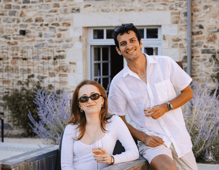 Two smiling people enjoy drinks outdoors at a historic stone building, ideal for a corporate retreat.