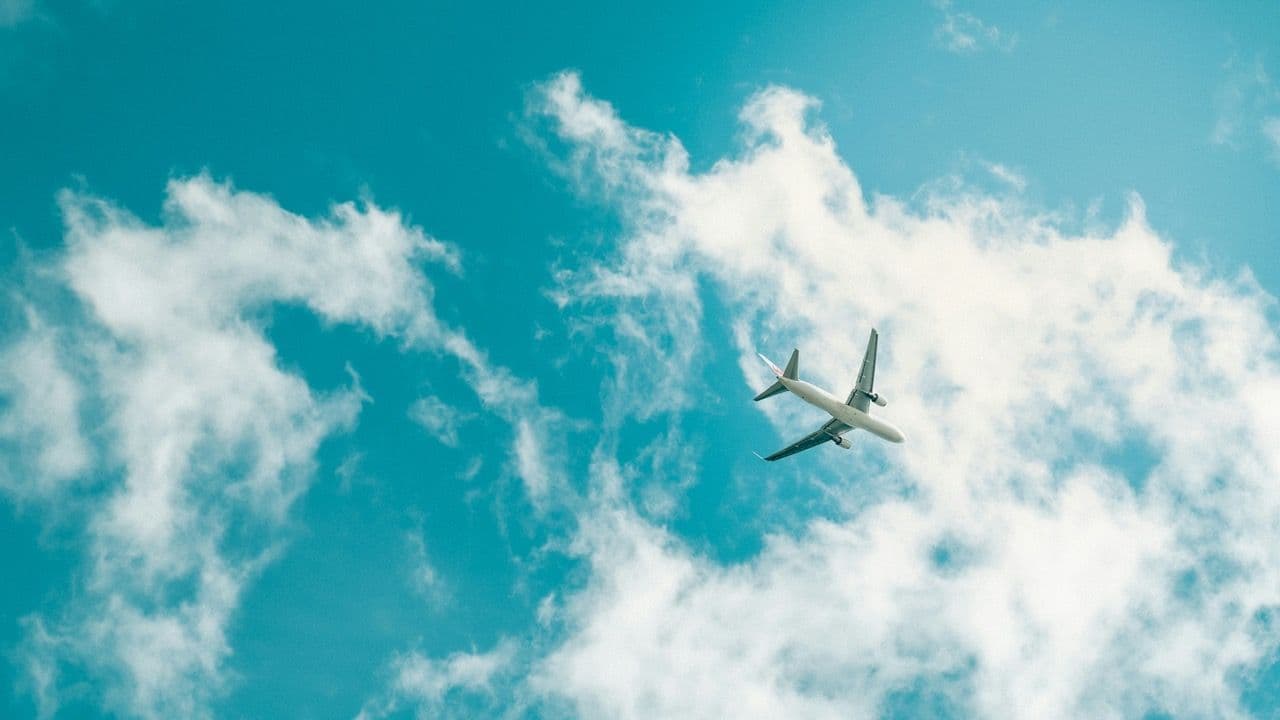 A white passenger airplane soars through a bright blue sky, perfect for corporate incentive trips.