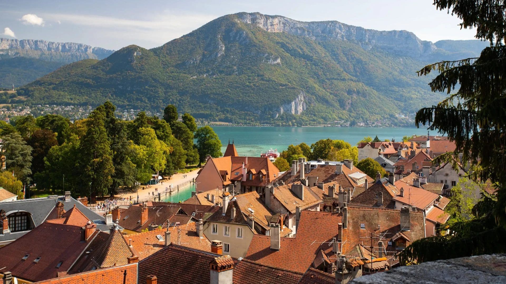 Scenic Annecy, France, featuring red-tiled roofs, a turquoise lake, and majestic forested mountains.