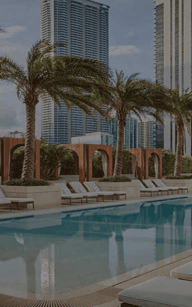 An outdoor event space featuring a swimming pool, lounge chairs, palm trees, and city skyscrapers.