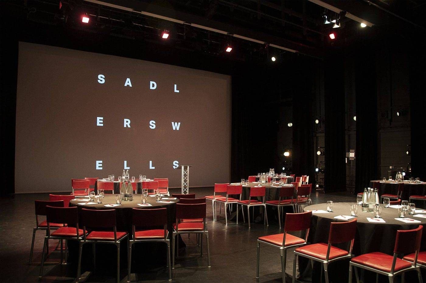 Auditorium at Sadler's Wells, London, set for a corporate seminar with round tables and a large screen.
