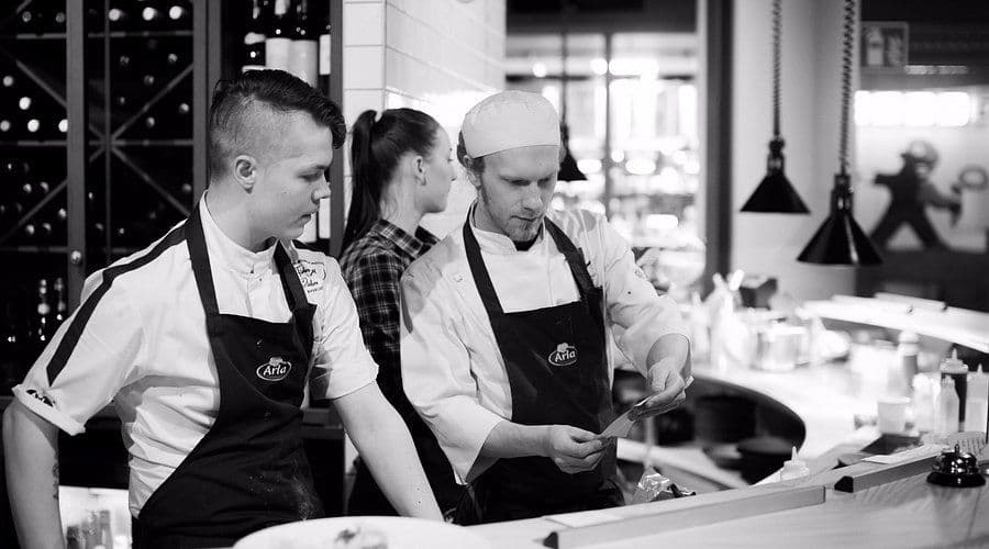 Two chefs prepare dishes in a professional kitchen, ideal for corporate dinner catering or a cooking class.