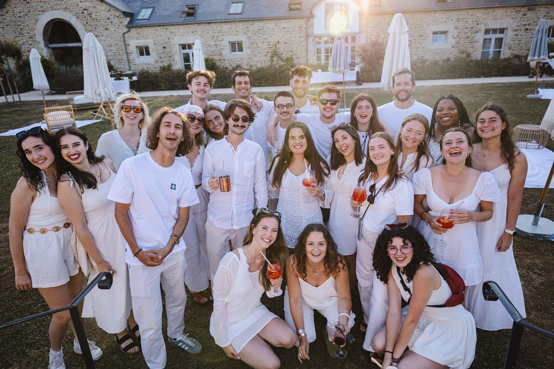 Smiling team members in white enjoy cocktails at a historic outdoor event venue during a company offsite.