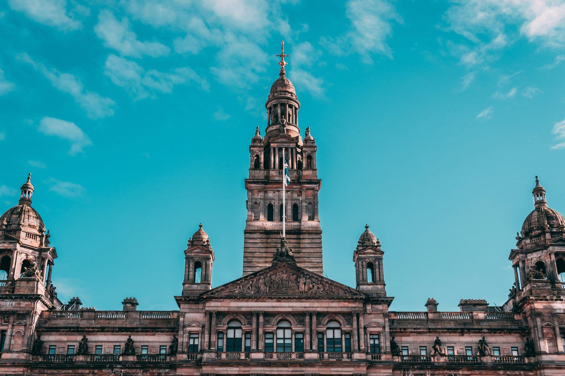 A grand historic building with a central tower and domes, featuring the Scottish flag
