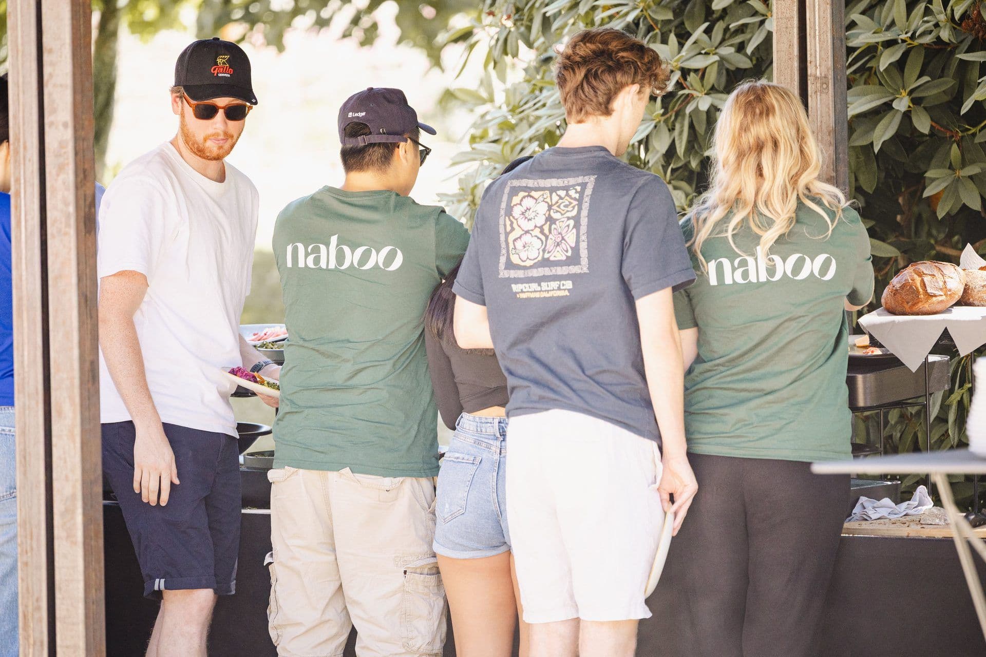 People in Naboo shirts queue for food at an outdoor corporate event, featuring a casual buffet setup.