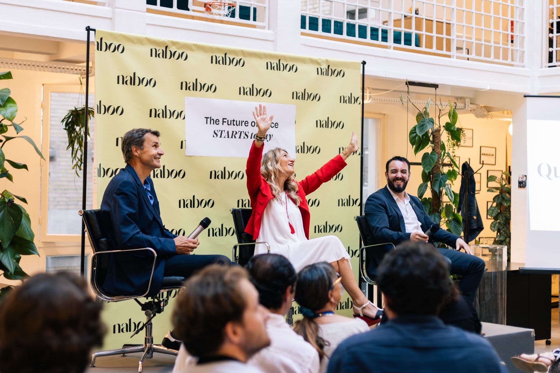 Three speakers on stage at a corporate seminar with a Naboo backdrop, engaging with an audience.