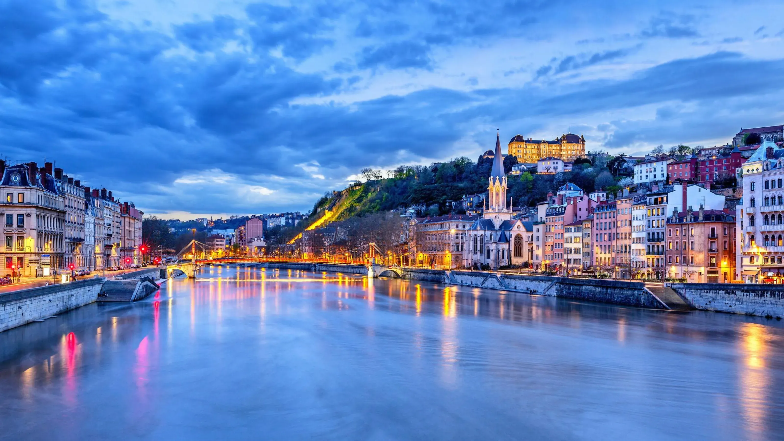 Illuminated Lyon cityscape at dusk with the Saône River, historic buildings, and Fourvière Basilica.