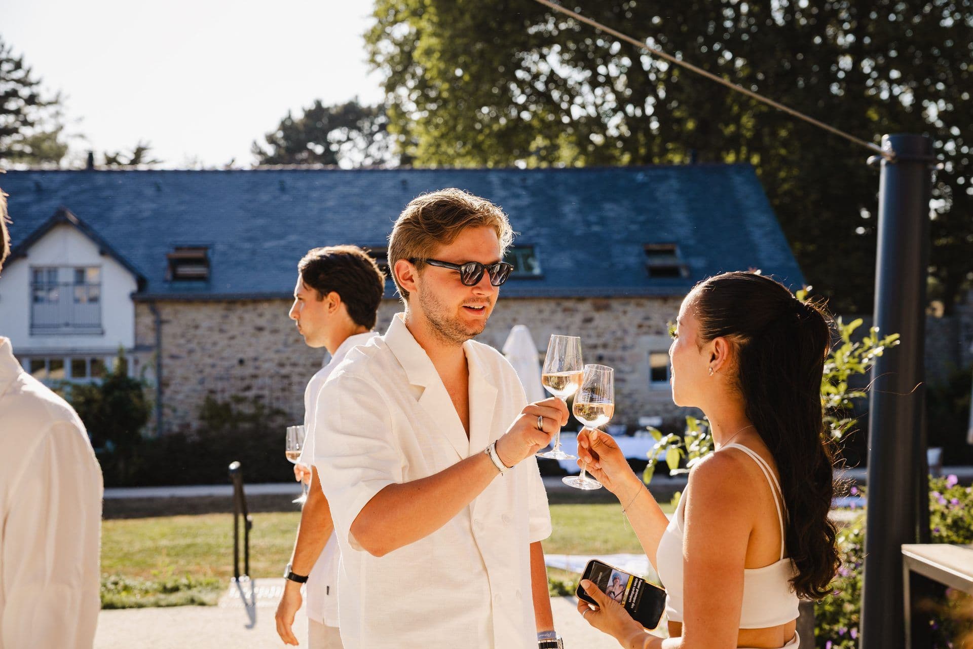 Two colleagues toast with wine glasses at an outdoor corporate event reception with a stone building in the