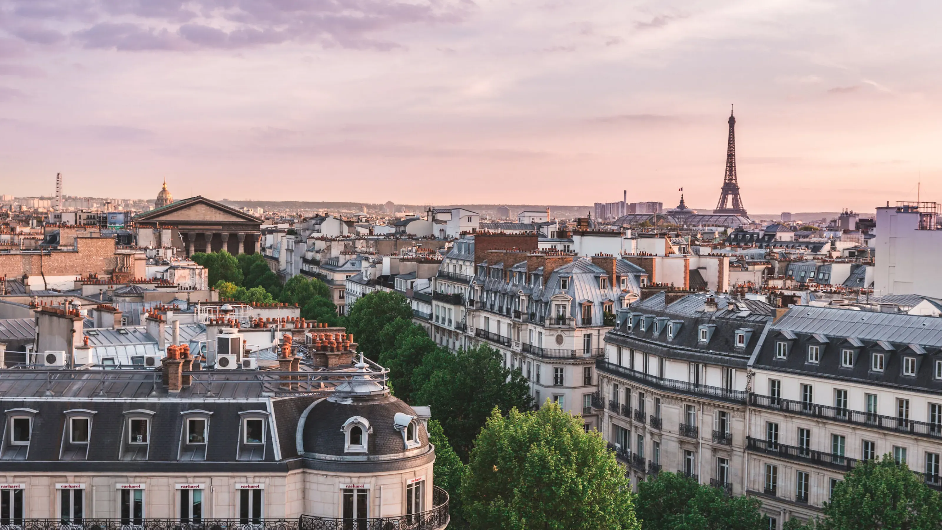 Rooftop view of historic Paris architecture with the Eiffel Tower under a soft sunset sky.