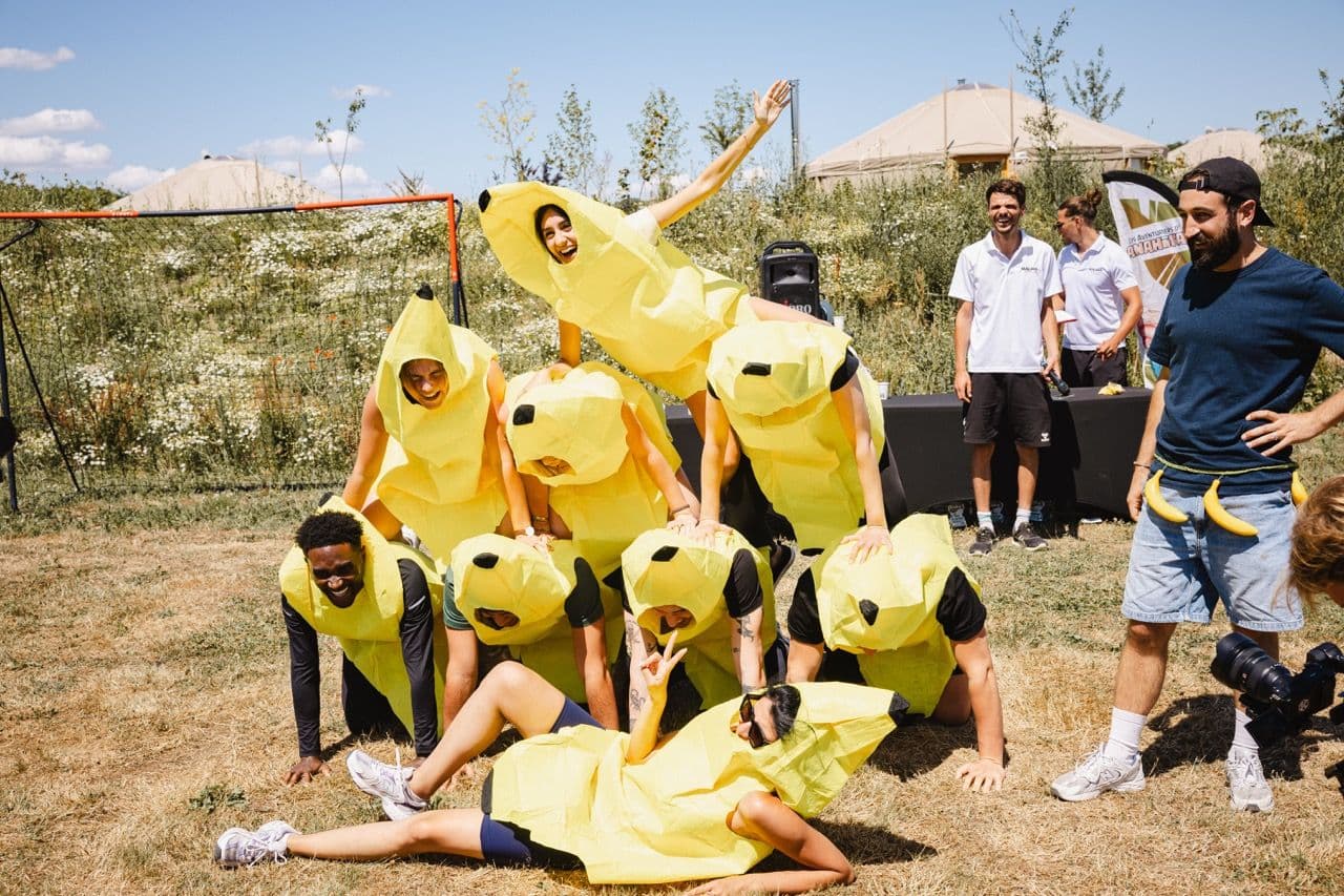 A team in banana costumes forms a human pyramid during an outdoor corporate team building activity.