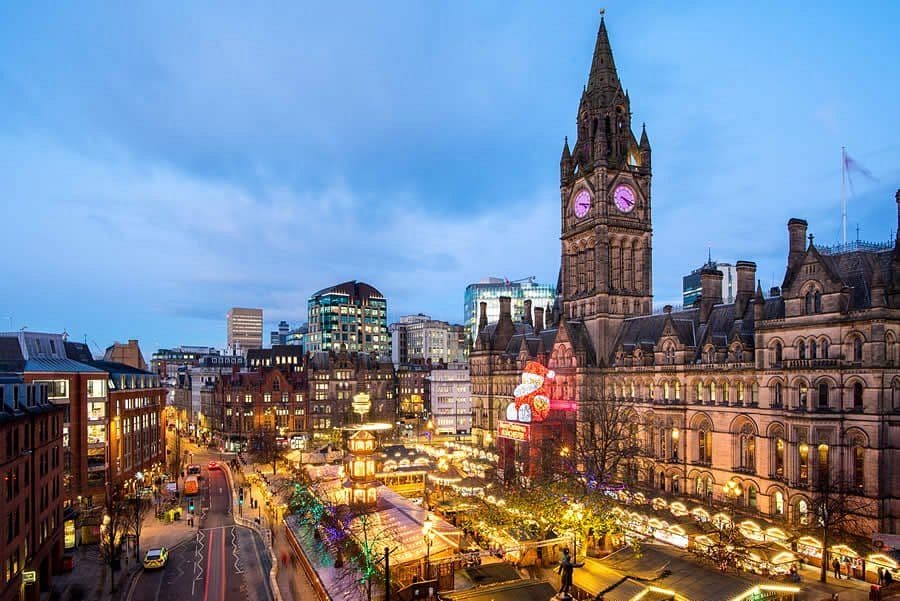 Historic Manchester Town Hall illuminated at dusk, overlooking a vibrant Christmas market.