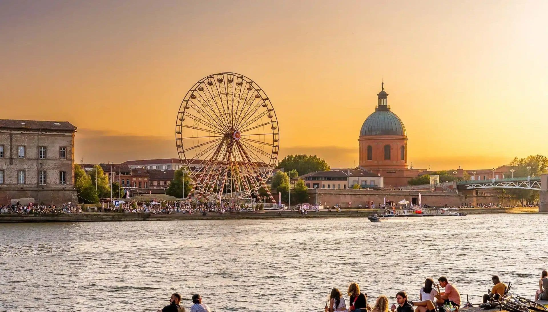Sunset over Toulouse, France, showing the Garonne River, a Ferris wheel, and historic Dôme de la Grave.