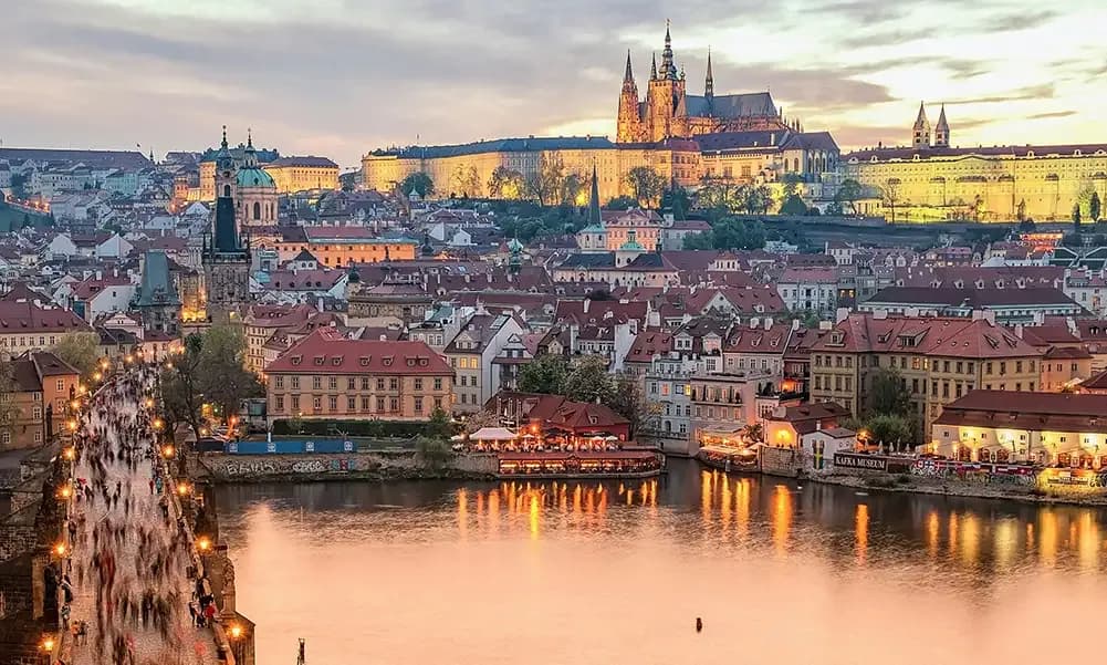Panoramic view of the illuminated Prague cityscape at dusk, featuring Charles Bridge, Vltava River